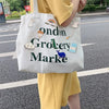 A white tote bag featuring text and various cute fashion pins, carried by a person in a yellow dress.