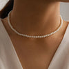 Gros plan d'un collier de perles minimaliste porté autour du cou sur peau lisse et tissu clair.