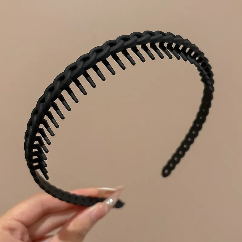 A black frosted toothed anti-slip hair headband is held by a hand against a neutral background.