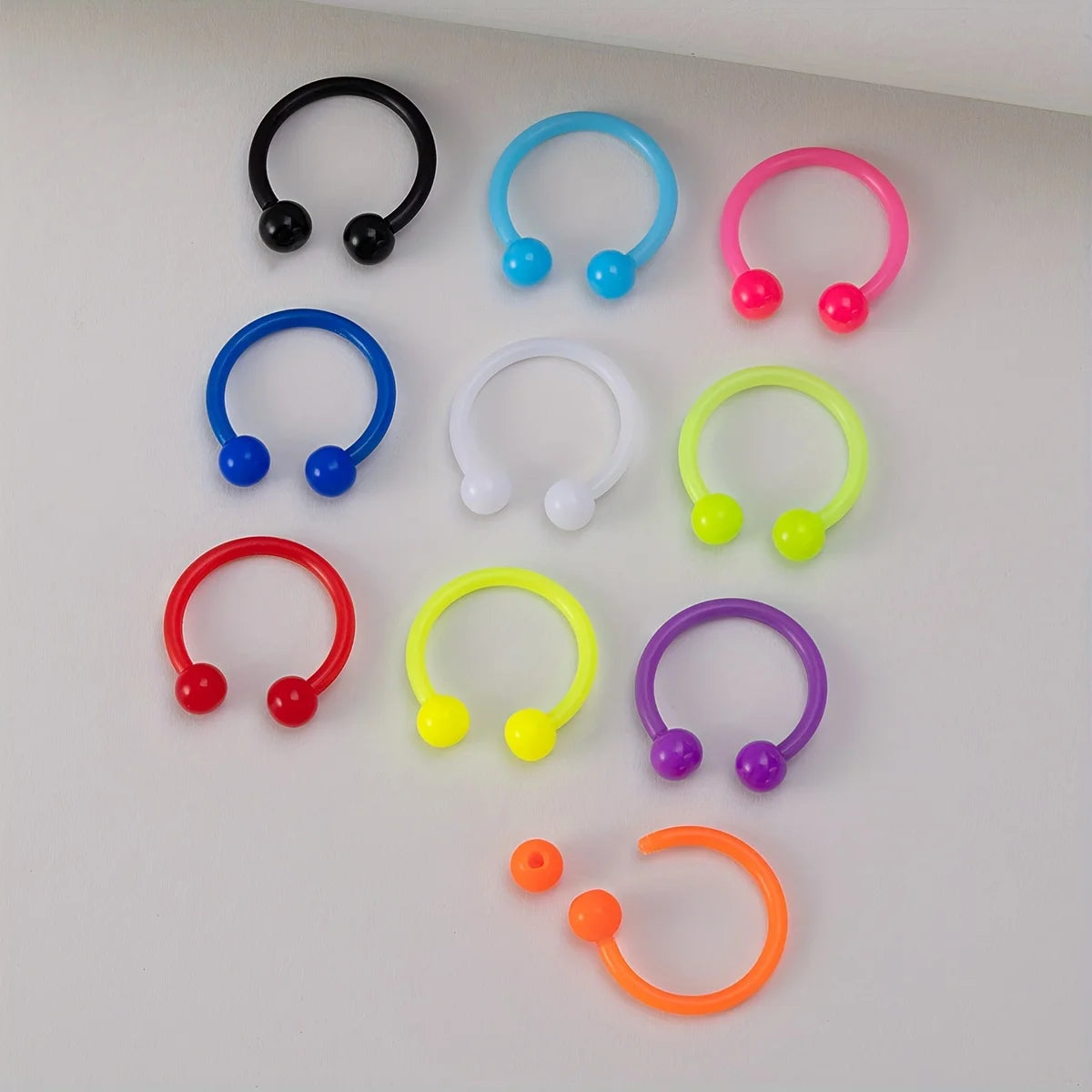 A collection of flexible acrylic piercing jewelry rings in various colors including black, blue, pink, green, red, and purple
