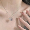 A close-up of a delicate silver heart necklace featuring pink zircon stones worn around the neck.