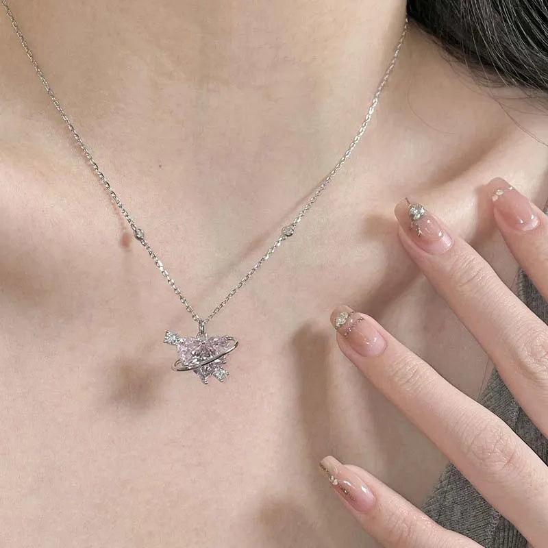 A close-up of a delicate silver heart necklace featuring pink zircon stones worn around the neck.