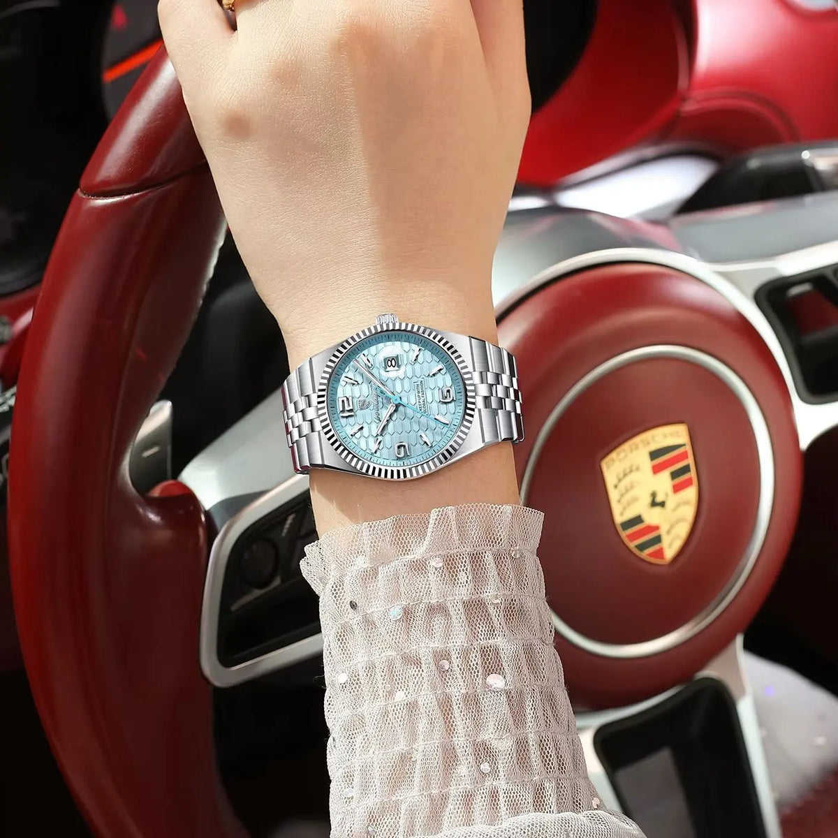 A close-up of a woman's wrist wearing a silver-toned luxury quartz wristwatch with a light blue luminous dial and a textured 