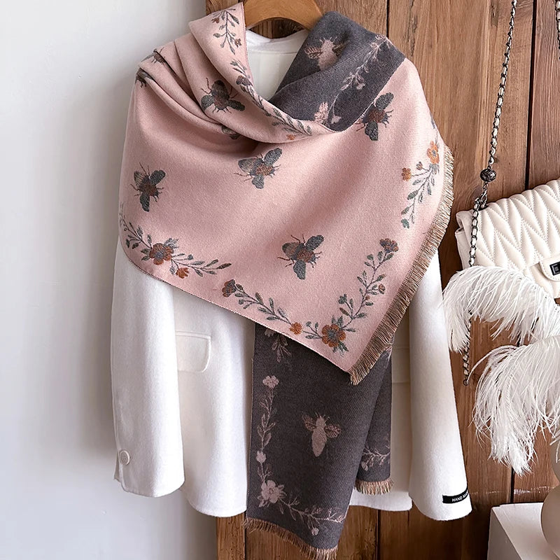 A pink and gray pashmina shawl with a floral bee print draped over a white blazer.