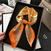 An orange and gold patterned silk scarf tied in a bow displayed in a black picture frame.
