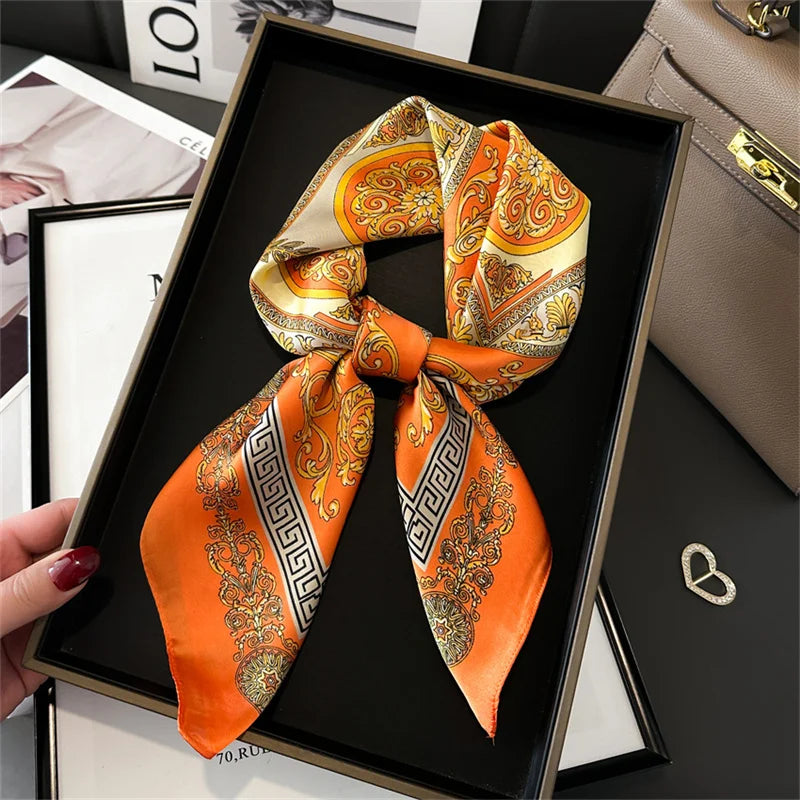 An orange and gold patterned silk scarf tied in a bow displayed in a black picture frame.