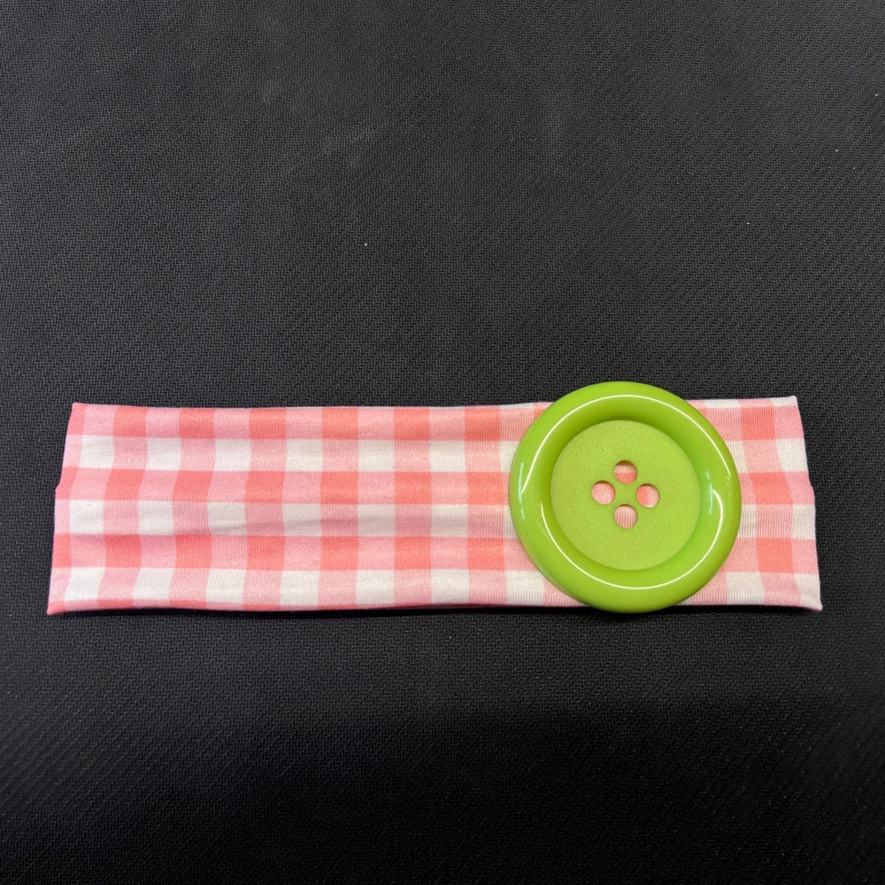 A pink checkered fabric headband with a bright lime green button attached.
