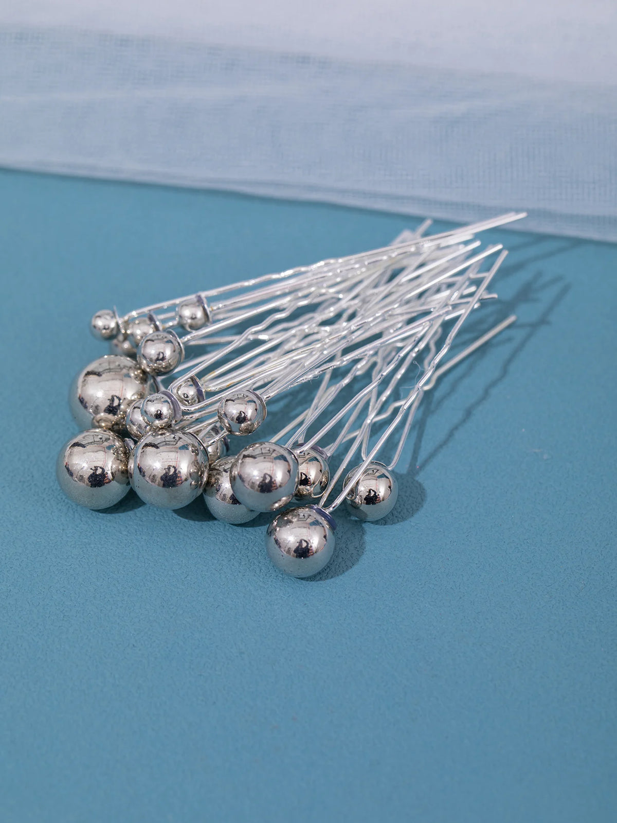 A collection of 18 silver faux pearl hair pins with thin wires arranged on a blue surface.