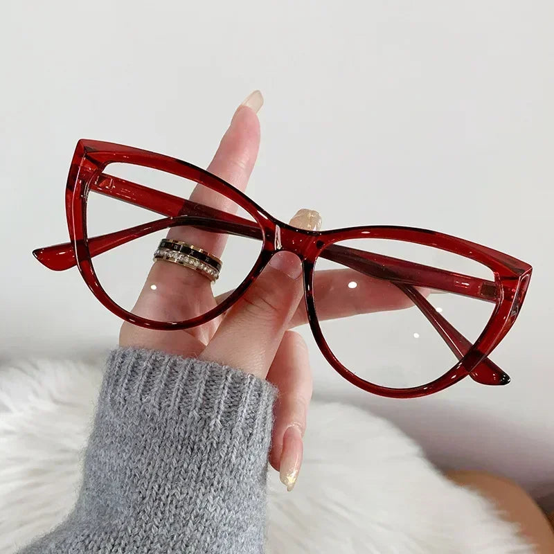 Eine Hand hält eine rote Vintage-Cat-Eye-Brille mit Goldakzenten vor einem weißen, flauschigen Hintergrund.