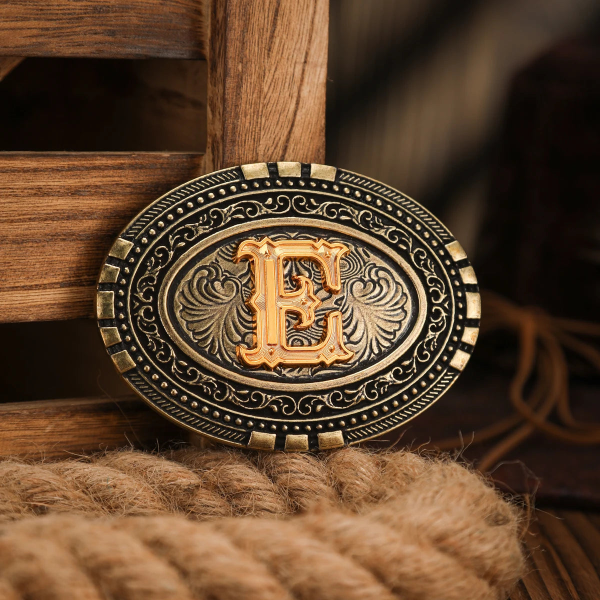A vintage gold-toned belt buckle with an embossed letter E is displayed on a wooden surface.