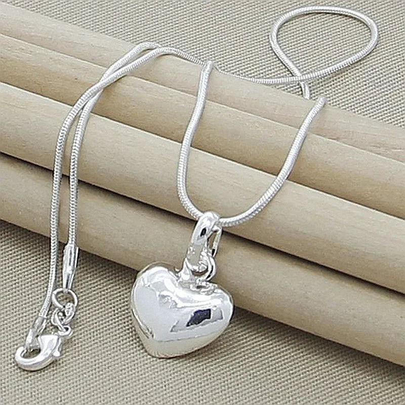 A silver heart snake necklace is displayed resting on a beige woven background.