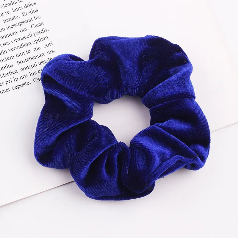 A close-up photo of a royal blue velvet scrunchie with gathered fabric texture.