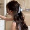 A woman with long dark hair is styling it with a set of light blue striped hair clips.