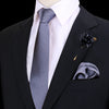 Chaqueta negra, camisa blanca, corbata gris a rayas, prendido floral oscuro y pañuelo de seda doblado.