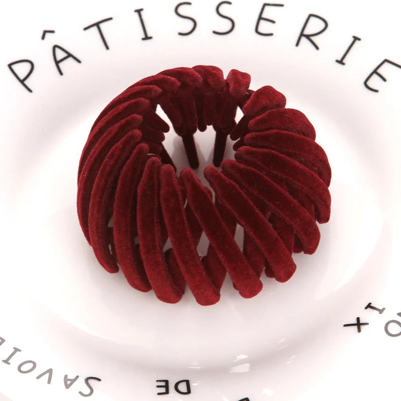 A close-up of a wreath of deep red velvet hair clips arranged on a white plate.