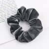 A close-up shot of a dark gray velvet scrunchie, showing its textured fabric and gathered design.