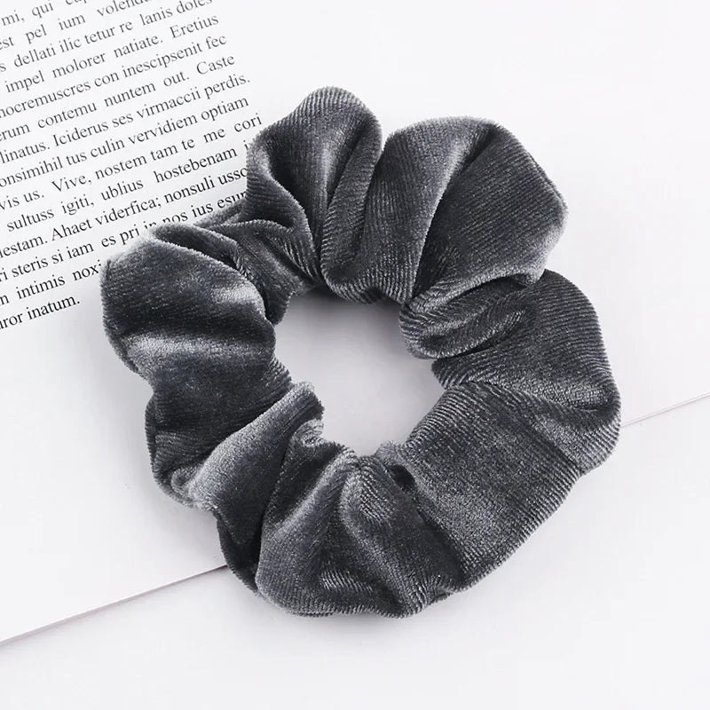 A close-up shot of a dark gray velvet scrunchie, showing its textured fabric and gathered design.
