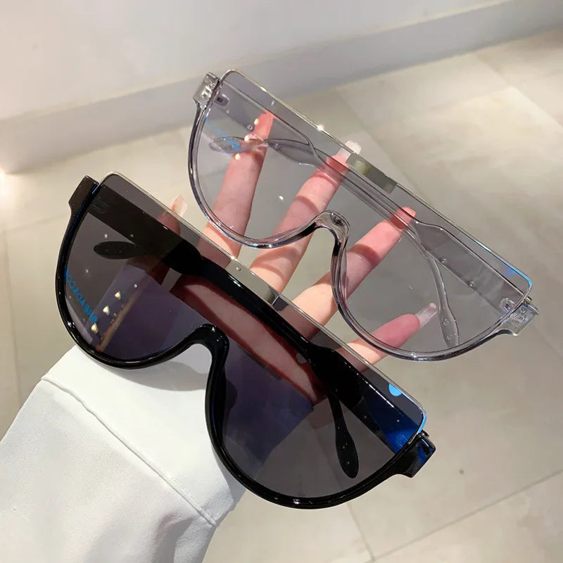 A pair of clear plastic vintage cat eye sunglasses with dark tinted lenses being held by a hand.