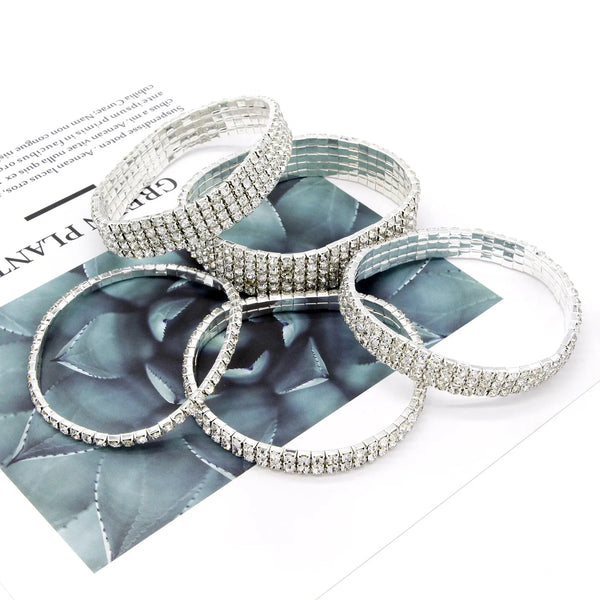 A stack of multi-layer crystal tennis anklets displayed on a dark patterned surface.