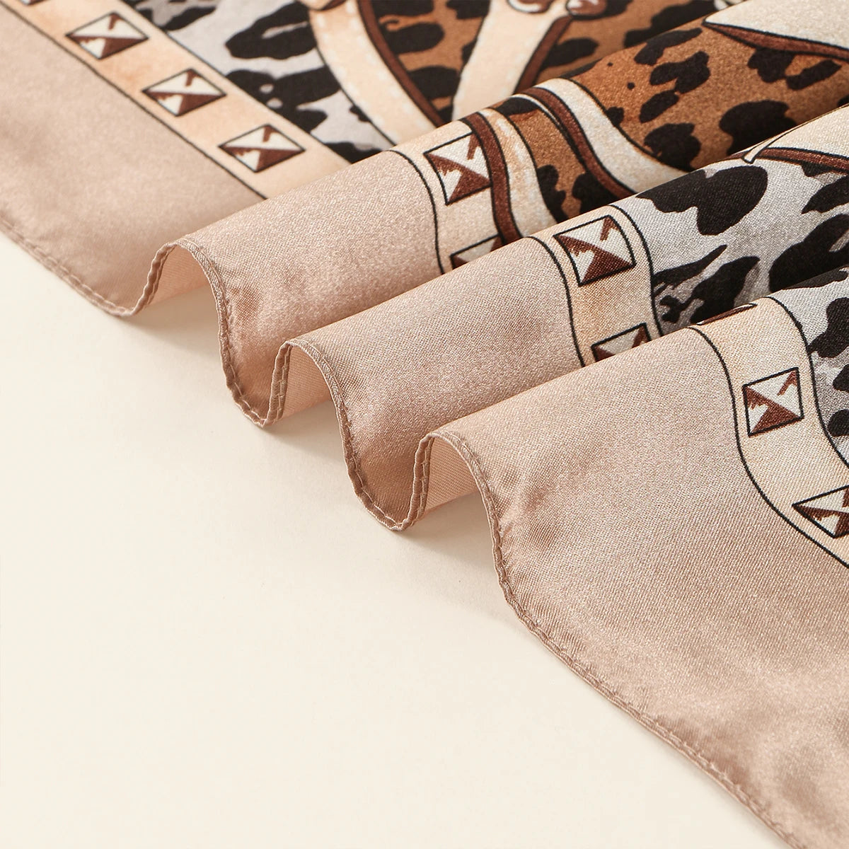 A close-up of a leopard print square satin scarf in brown and beige tones, showing the fabric texture and decorative stitchin