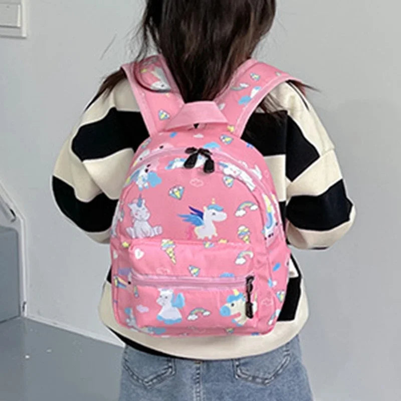 A pink backpack featuring a cute dinosaur and unicorn pattern worn by a person.
