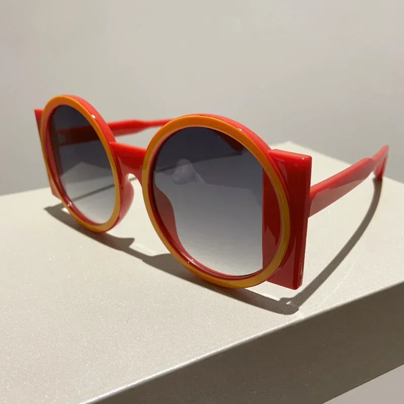 A pair of round double color fashion sunglasses with red and orange frames resting on a white surface.