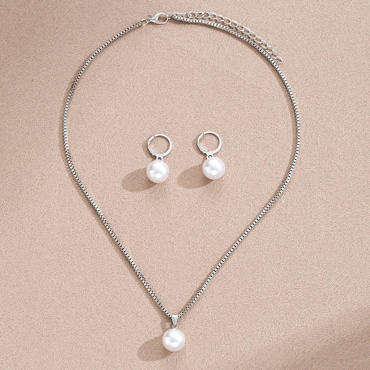 A delicate silver pearl jewelry set featuring matching dangle earrings and a pendant necklace.