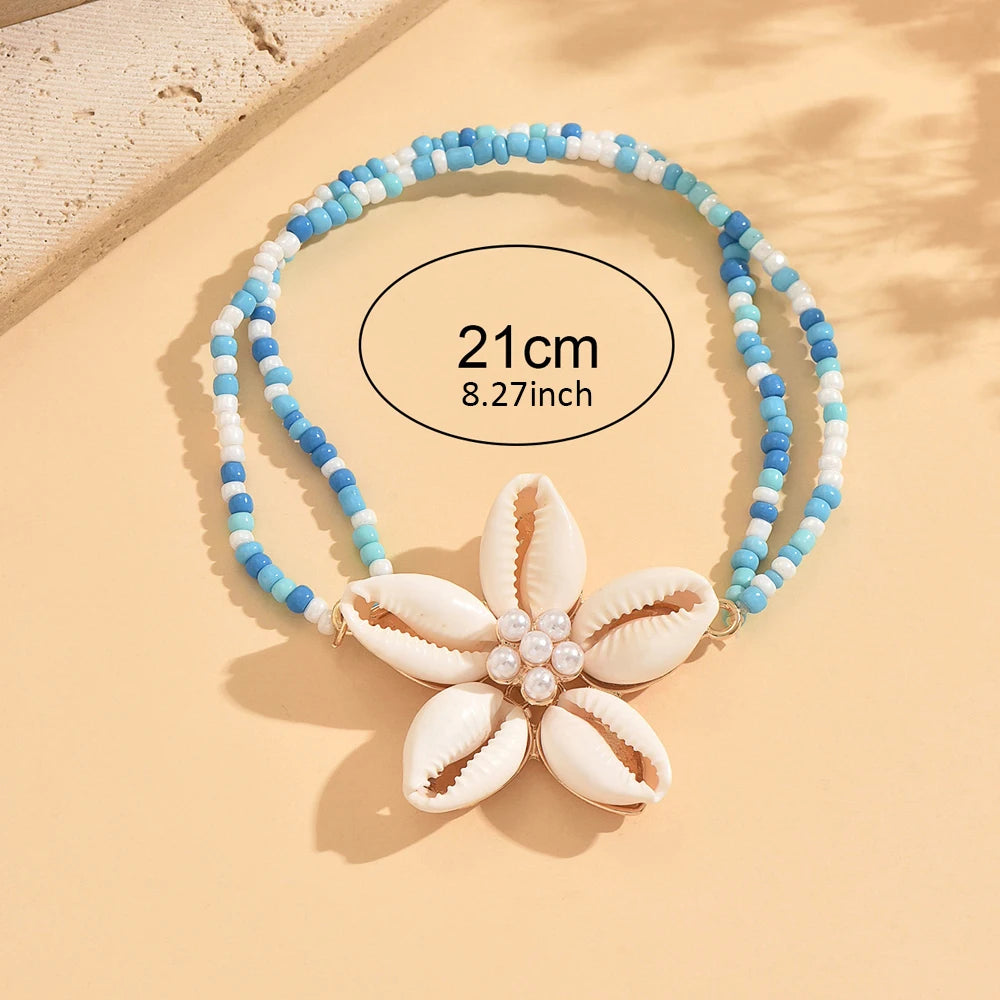 A white and blue beaded anklet featuring a flower-shaped cowrie shell charm.