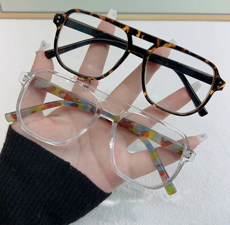 Una mano sostiene unas gafas de lectura estilo piloto vintage con monturas de marfil y detalles de varios colores.