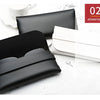 A black leather eyeglass case is shown open, next to a white card, with a white ceramic object in the background.