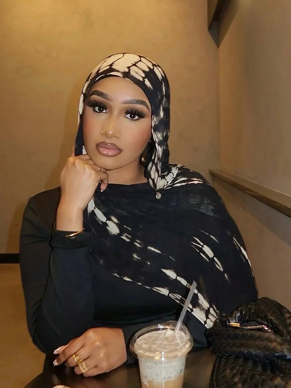 A woman wearing a black and white bohemian crocodile print hijab scarf, looking directly at the camera.