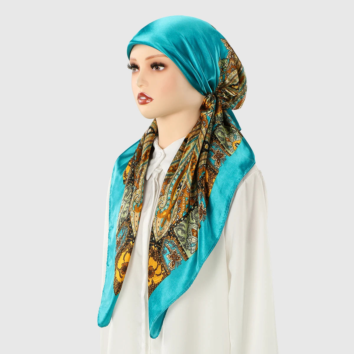 A woman wearing a teal satin silk hijab with an ornate patterned fabric tied around her neck.
