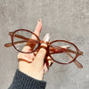A hand holds a pair of round, translucent brown computer glasses against a gray background.