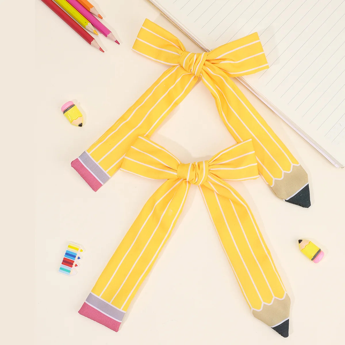 A set of yellow and pink striped fabric bows shaped like pencils, used as hair clips.