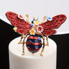 Broche baroque d'abeille et d'insecte détaillée avec des ailes rouges, des accents dorés et des éléments floraux bleus et jau