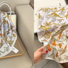 A light floral print silk scarf featuring orange and yellow accents displayed on a wooden tray.