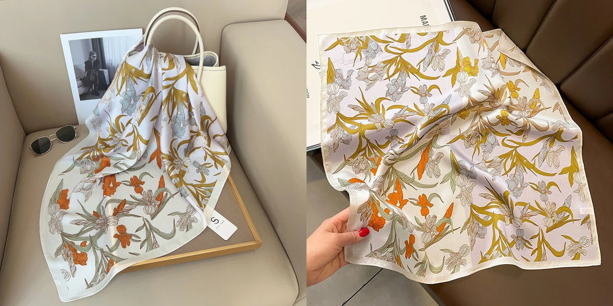 A light floral print silk scarf featuring orange and yellow accents displayed on a wooden tray.
