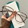 A pair of brown tortoiseshell retro anti-blue light sunglasses resting on a white card against a teal background.