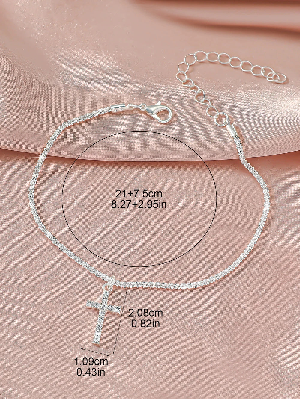 A delicate sparkling zircon heart cross anklet is displayed on a pink fabric with size measurements.