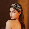 A young woman wearing an elegant pearl hair net headband, looking to the side against a warm brown background.