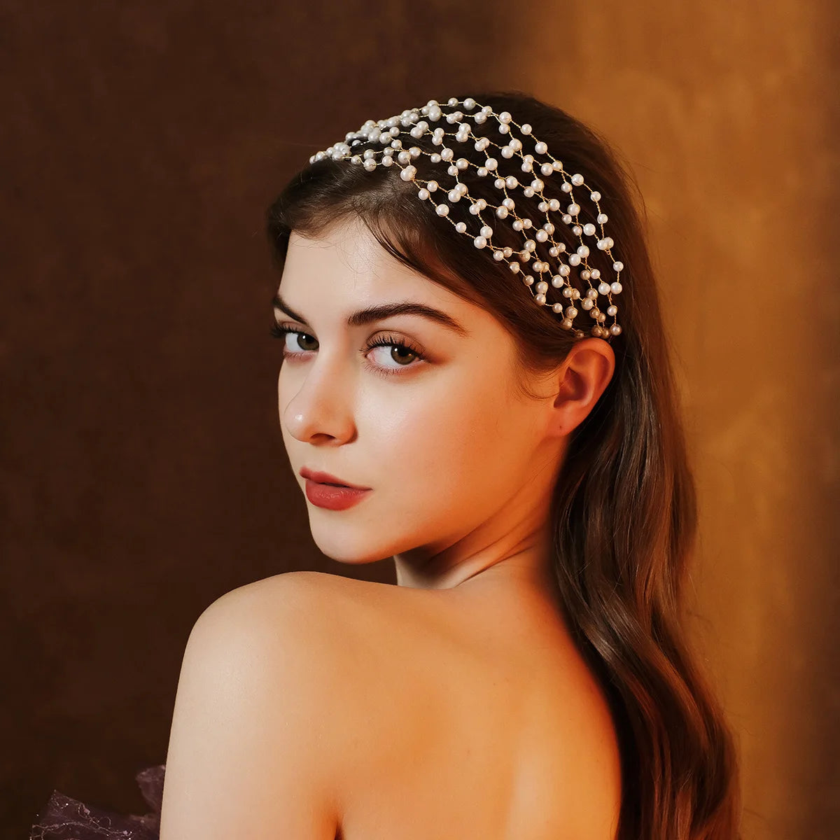 A young woman wearing an elegant pearl hair net headband, looking to the side against a warm brown background.