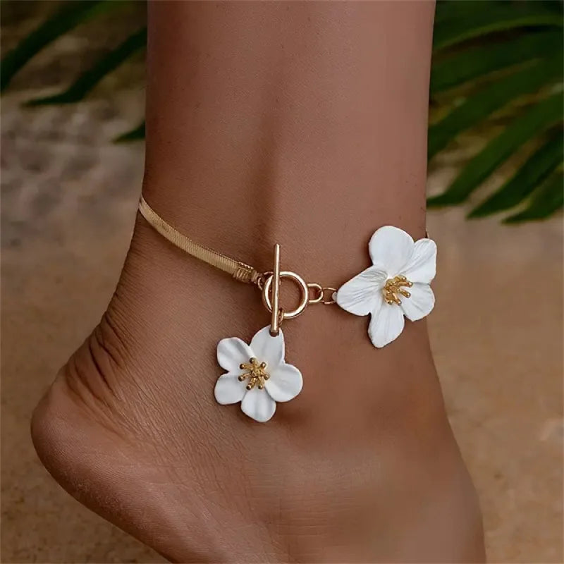 A gold chain anklet with white flower pendants worn on a person's ankle.