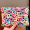 A hand holds a clear plastic bag filled with colorful elastic hair bands for girls in various shades of pink, purple, and yel
