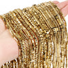 A hand holds several strands of gold-plated hematite round cube beads for DIY jewelry.