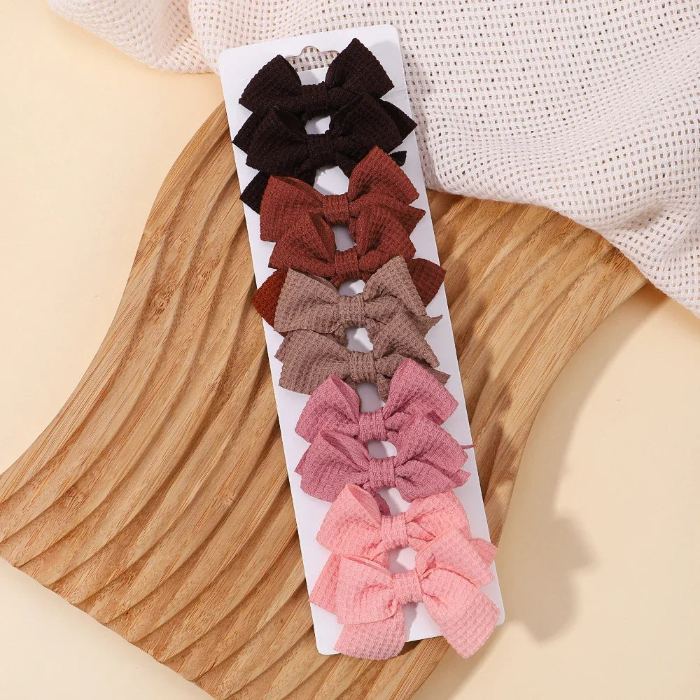 A display of nine handmade ribbon bow hair clips in various shades of brown, pink, and black arranged on a wooden board.