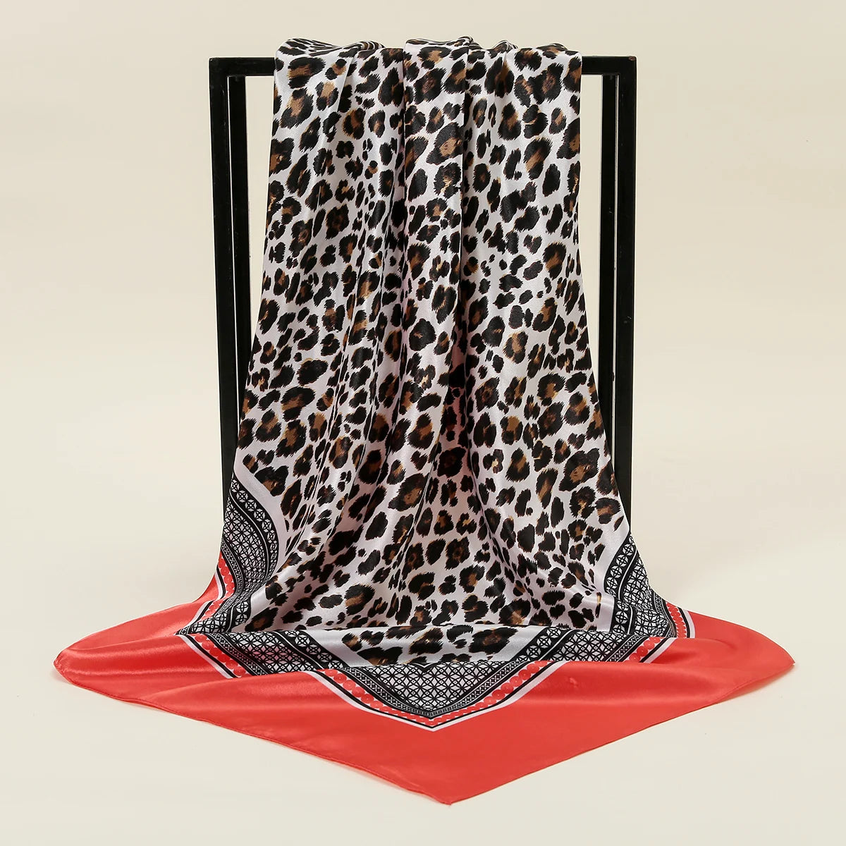Leopardmuster-Seiderschal aus Satin, drapiert auf einem schwarzen Displayständer auf roter Oberfläche.