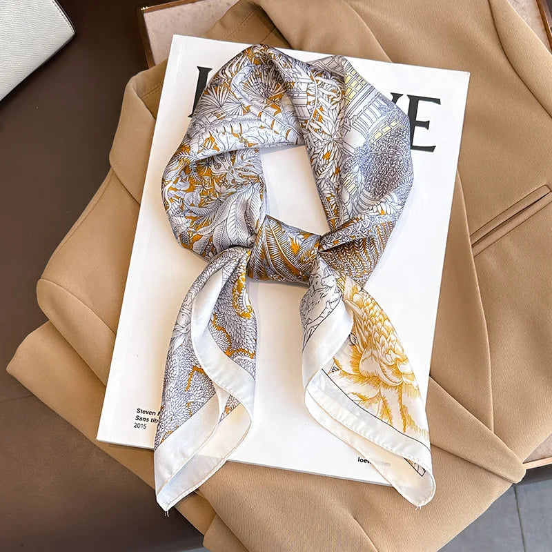 A patterned silk scarf tied in a knot, displayed on a white card against a beige blazer.