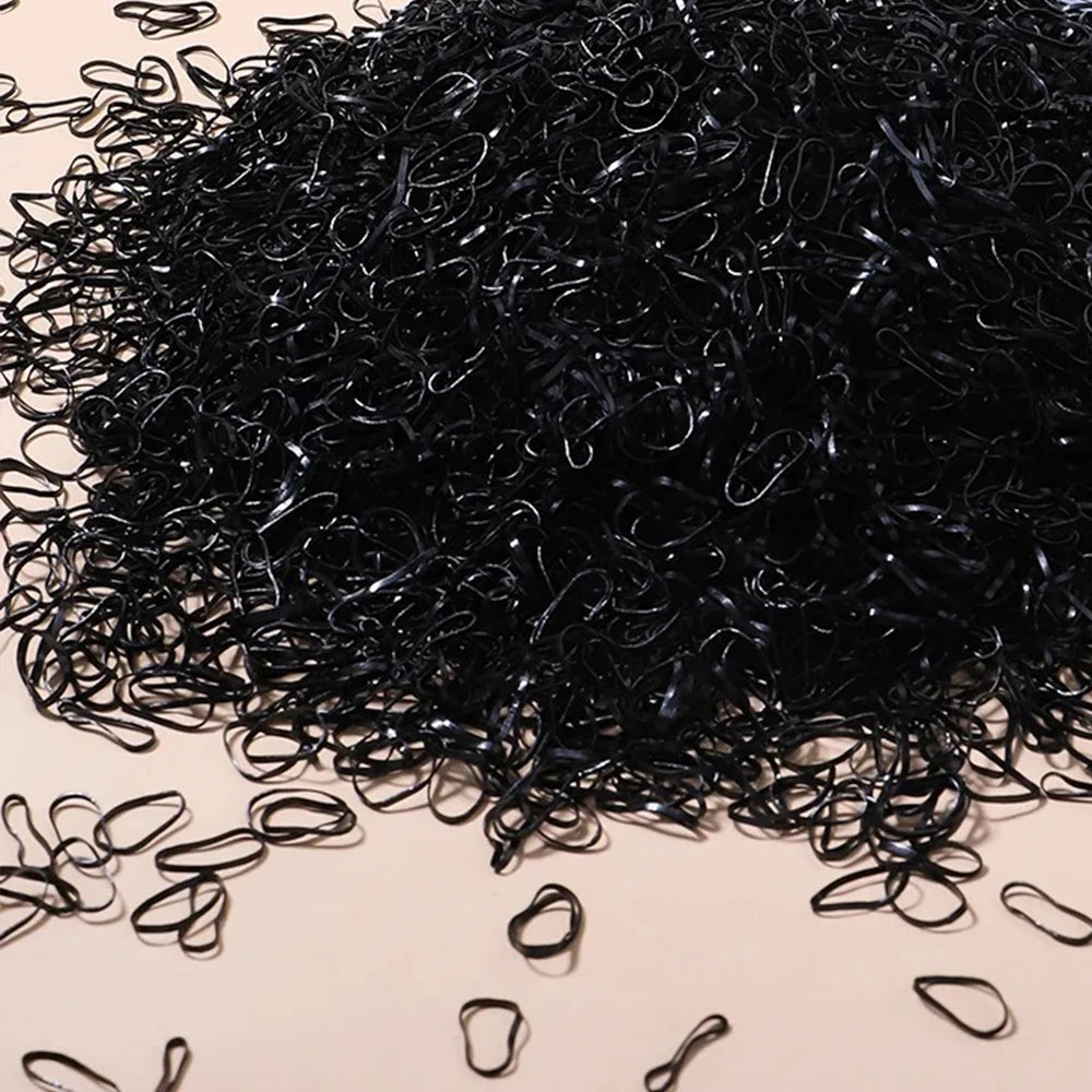 A pile of black disposable rubber hair ties scattered on a light surface.