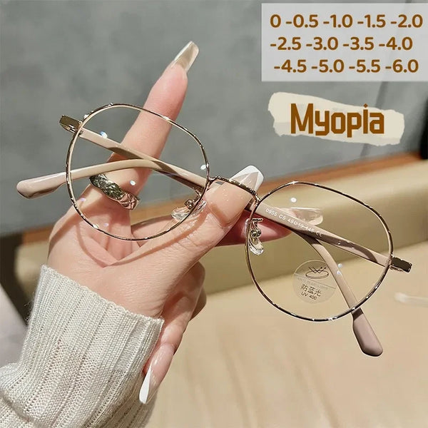 A hand holds a pair of thin, wire-rimmed eyeglasses with light brown frames and clear lenses against a blurred background.