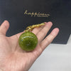 Une main tient un porte-clés de forme de poire verte cristalline avec une chaîne dorée sur fond sombre.